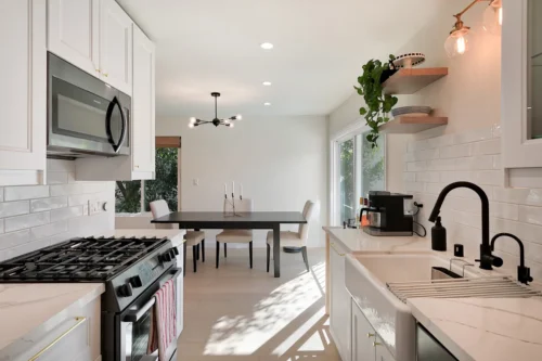 Modern Kitchen With White Cabinets, Black Fixtures, A Gas Stove, And Dining Area Basking In Natural Light From Large Windows—perfect Inspiration For Your Bathroom Remodeling Project.