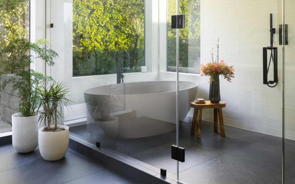 bathroom remodel contractor Modern bathroom, expertly crafted by a skilled bathroom remodel contractor, features a freestanding tub, large windows, potted plants, and a small wooden table with a floral arrangement.